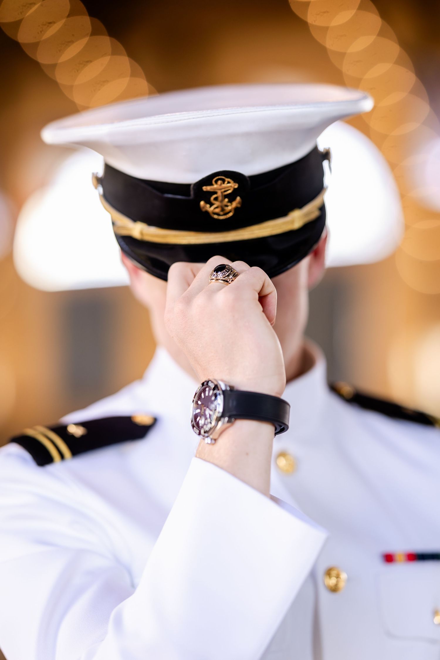Naval officer in white dress uniform adjusting cap, wearing a luxury watch with bokeh background.