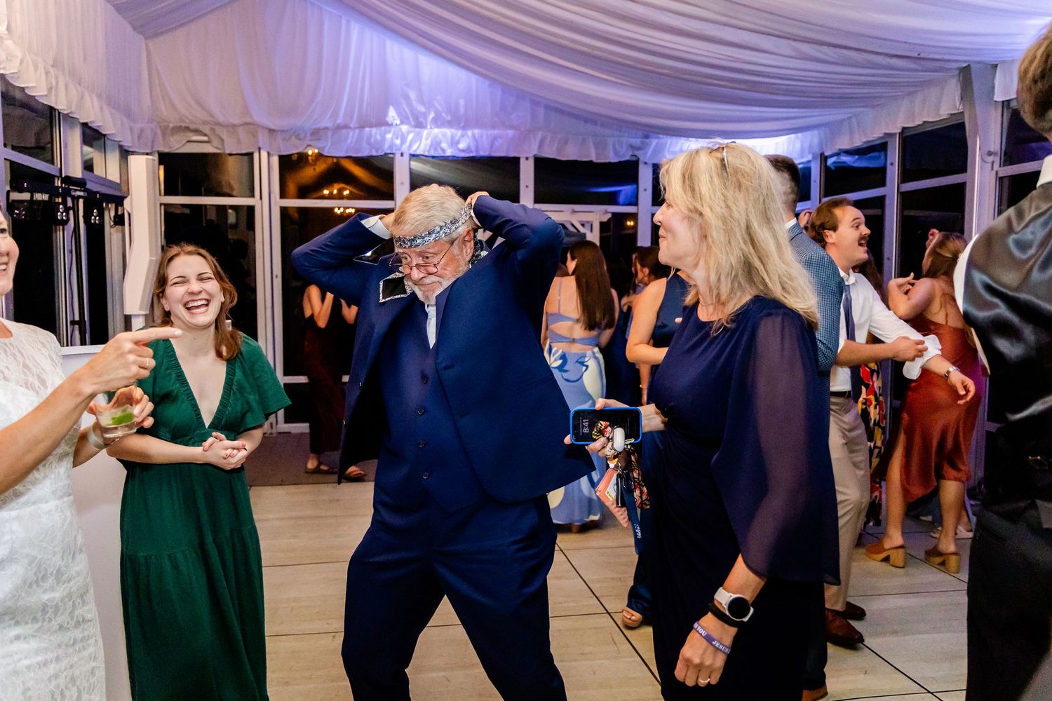 Wedding guests dancing and celebrating at an indoor reception with draped ceiling decor.