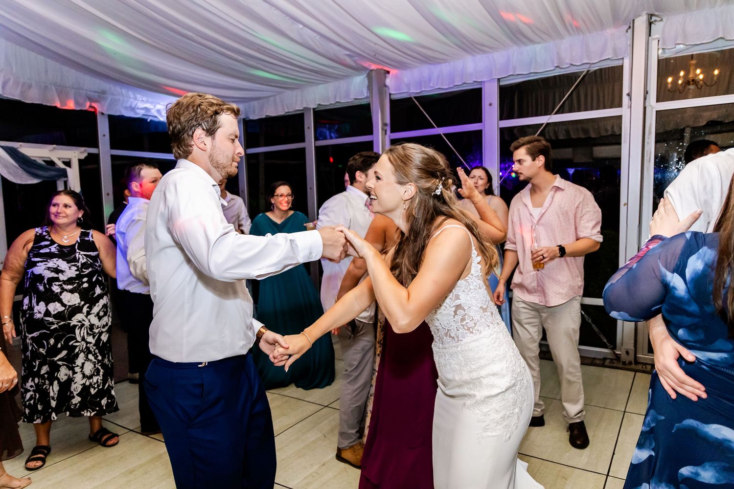 Wedding reception dance floor filled with guests celebrating under purple-lit tent draping.