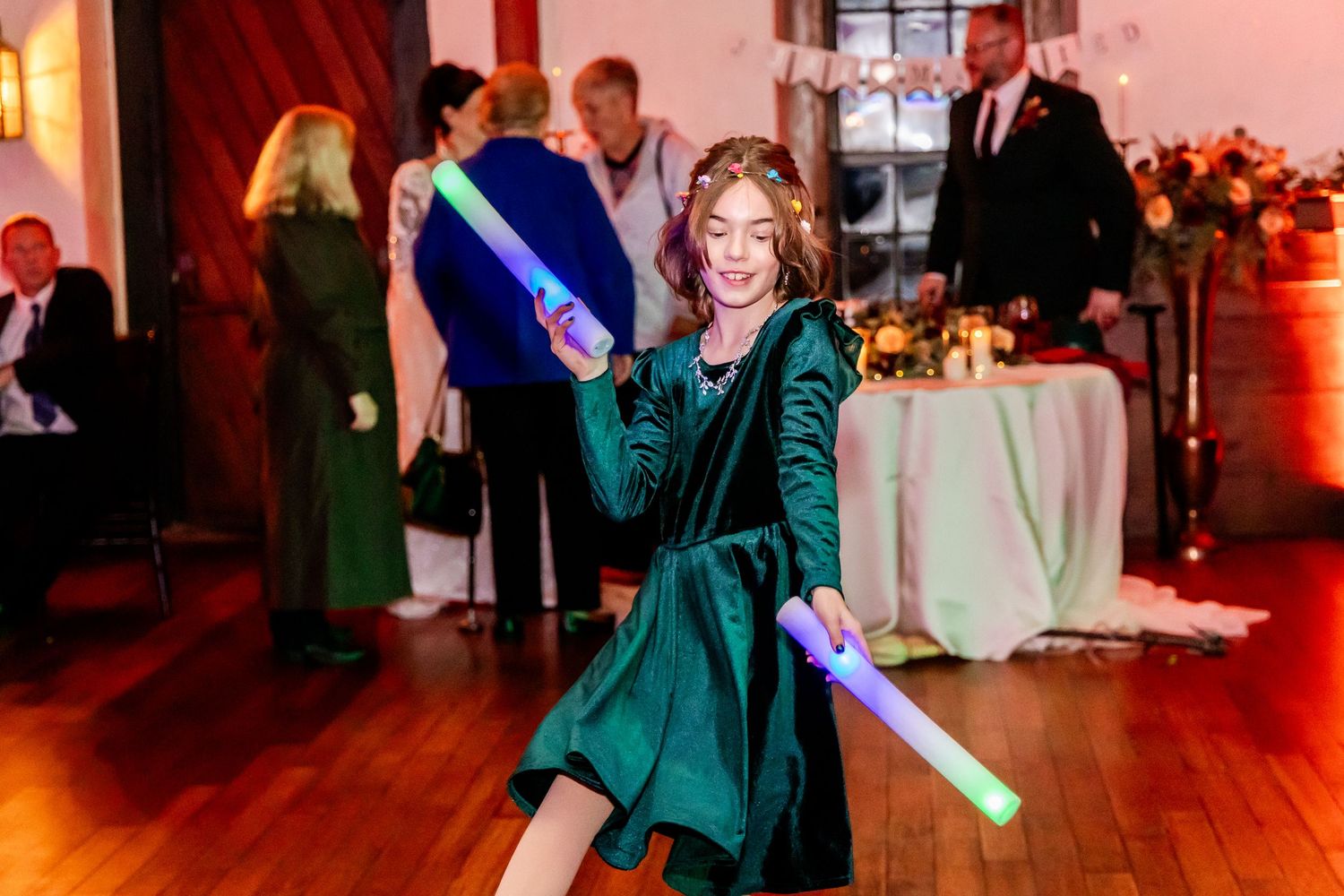 Party guest in velvet green dress dancing with light-up foam stick at reception.
