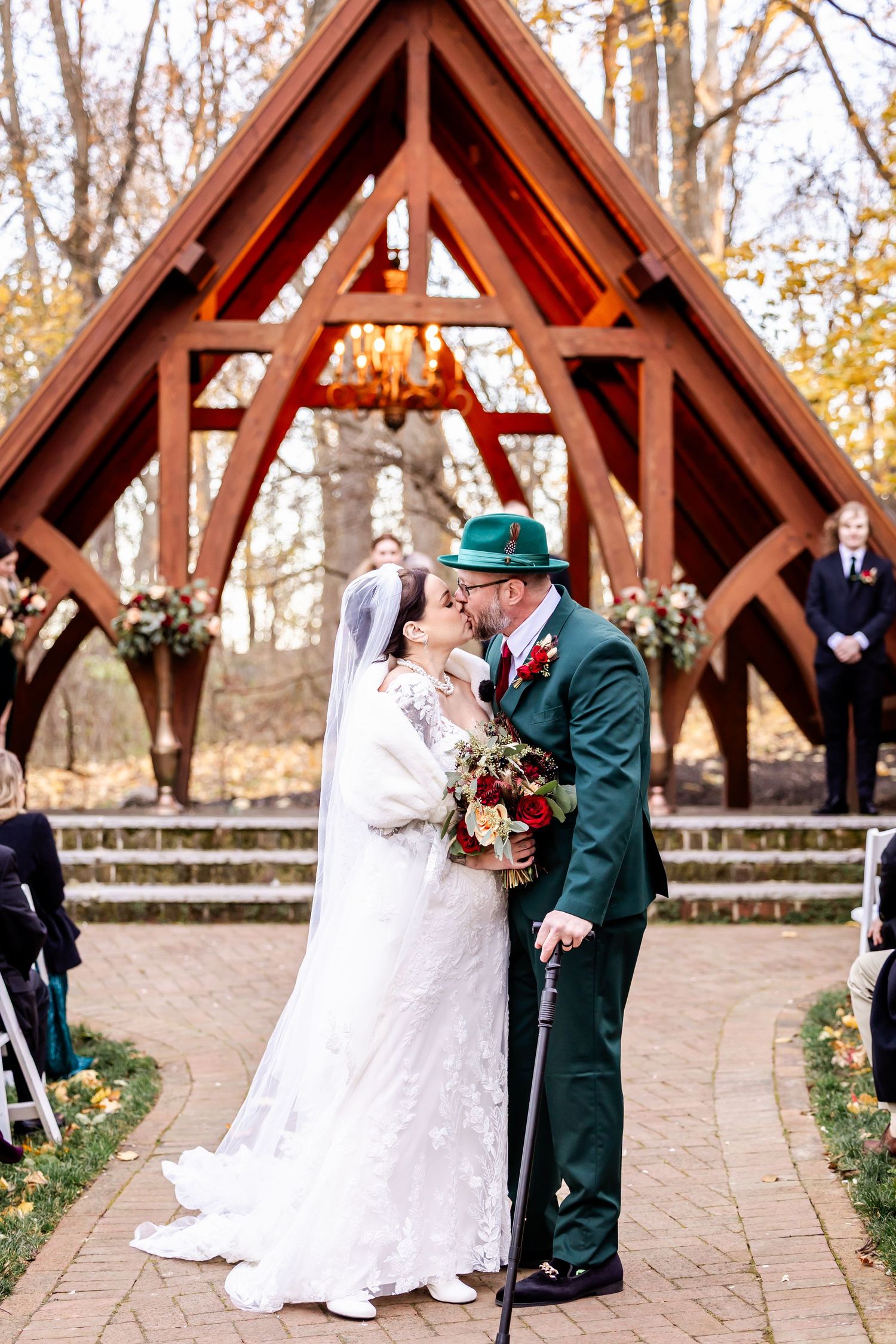 A couple shares a romantic moment under a wooden pavilion during their outdoor autumn wedding ceremony.