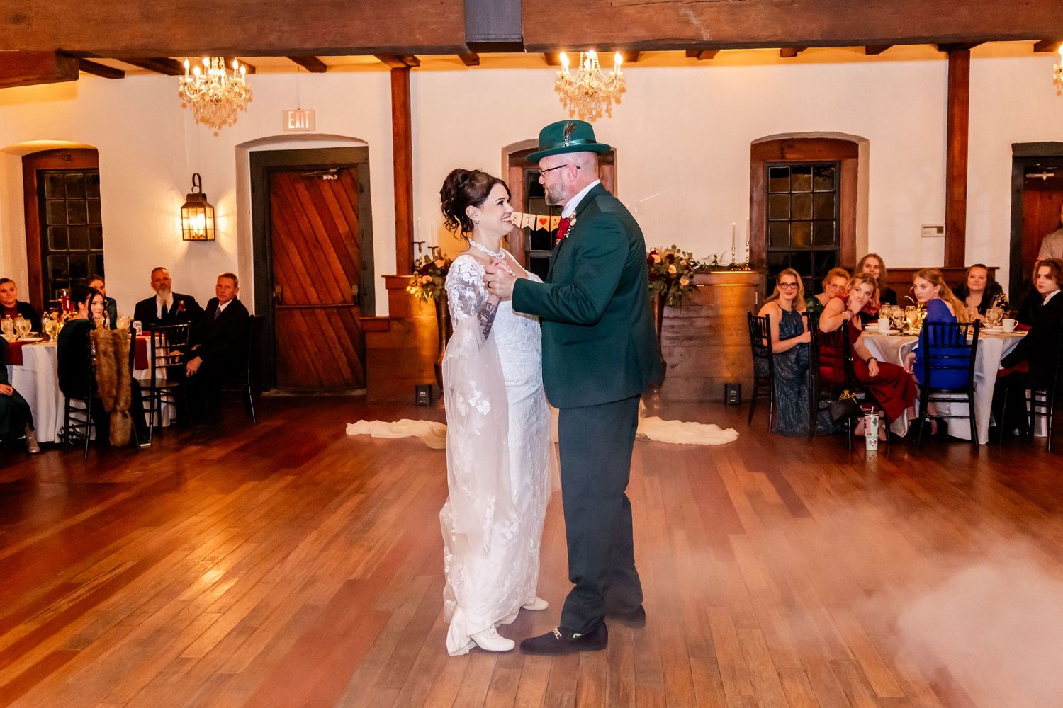Couples dancing on a wooden dance floor at an indoor wedding reception with warm lighting.