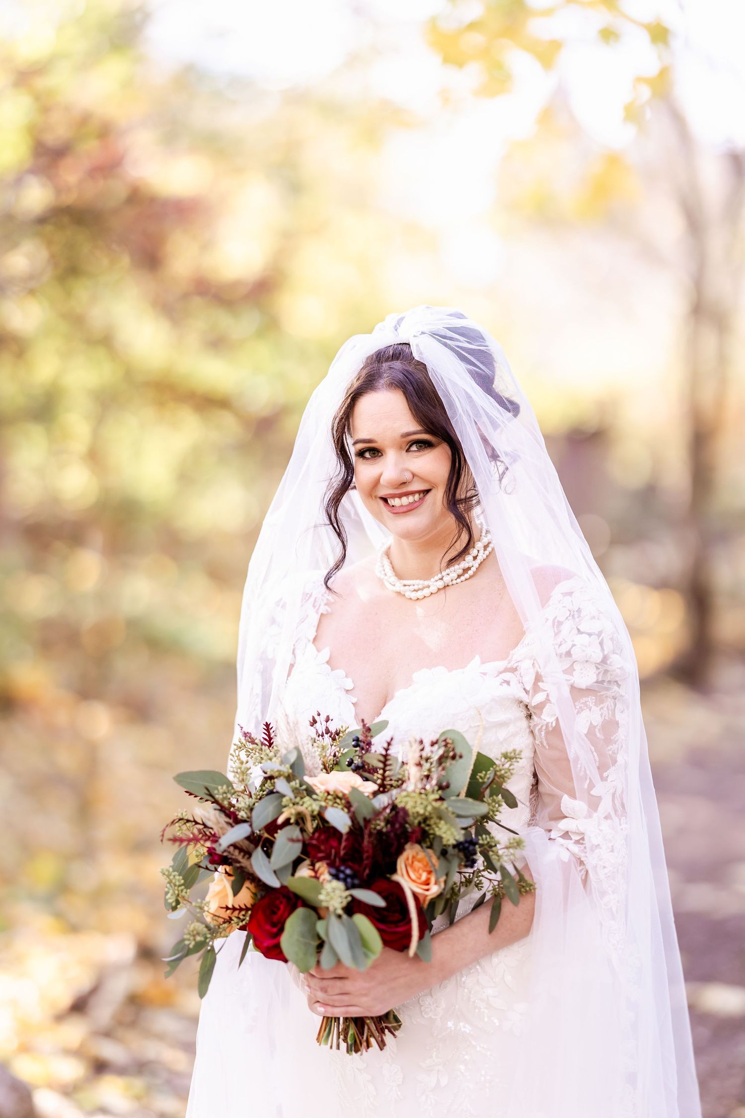 Beautiful autumn wedding bouquet with red and peach flowers held by bride in white lace dress and veil.