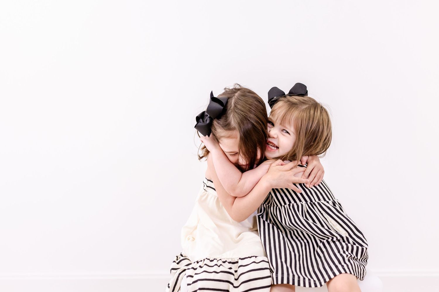 Two children in black and white striped dresses hug and laugh against a white background.