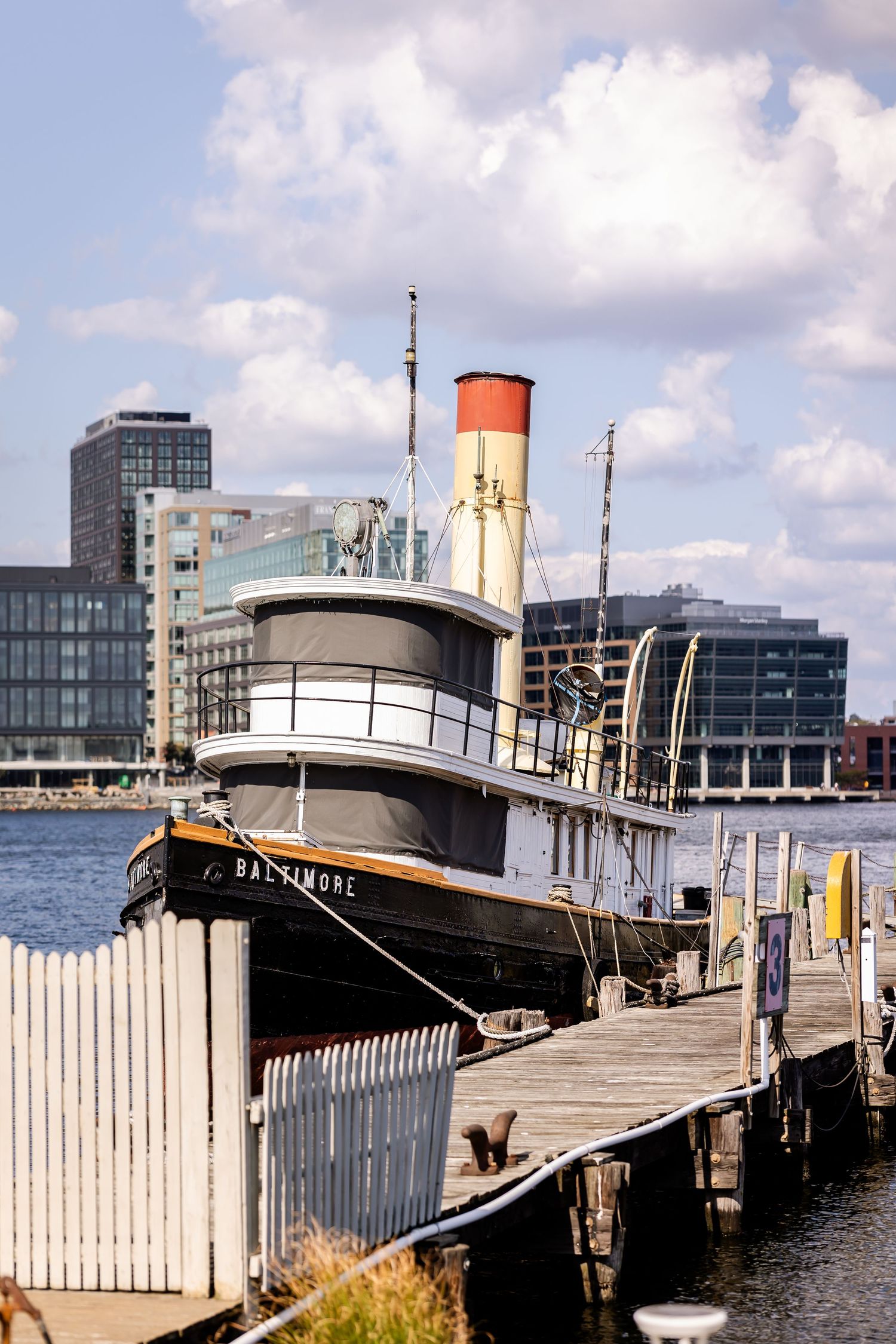 Vintage tugboat moored at a waterfront dock with modern buildings in the background.