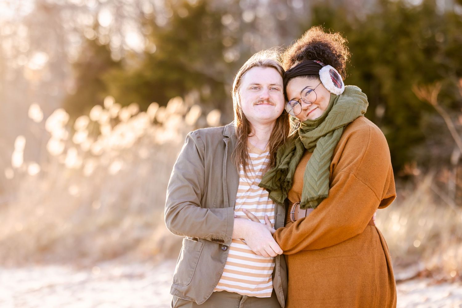 Two people embracing and laughing in warm winter clothing during sunset.