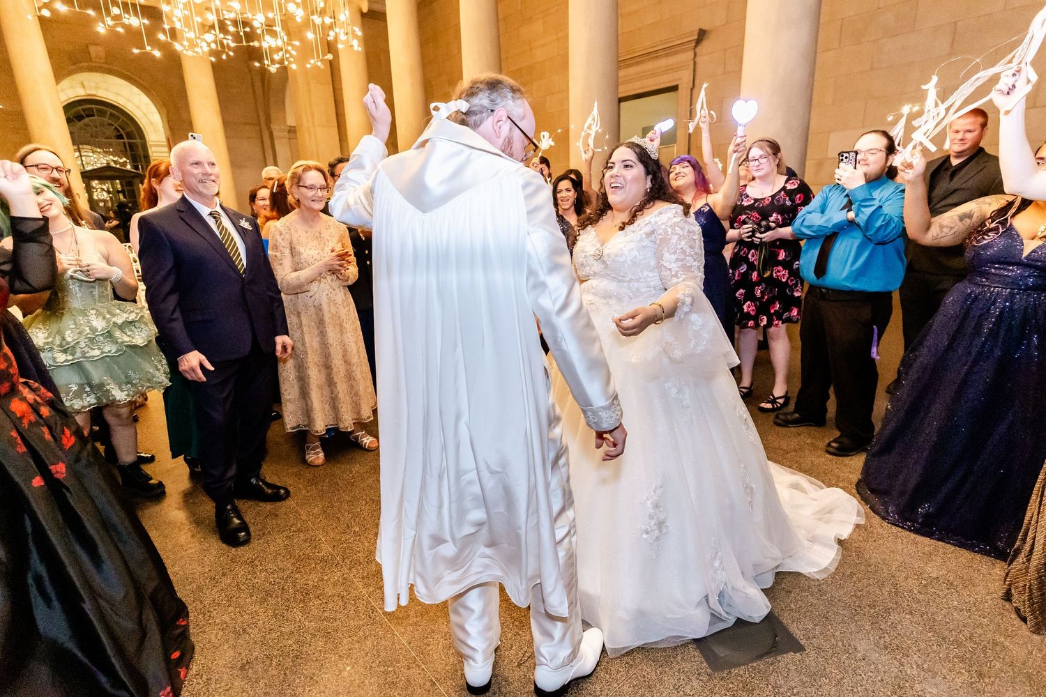 Wedding guests watch and celebrate as the couple dances in an elegant venue with chandeliers.