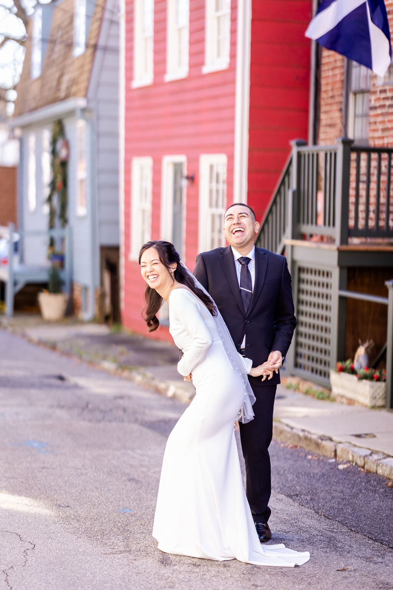 A playful wedding photoshoot taking place on a street with red buildings and brick architecture.