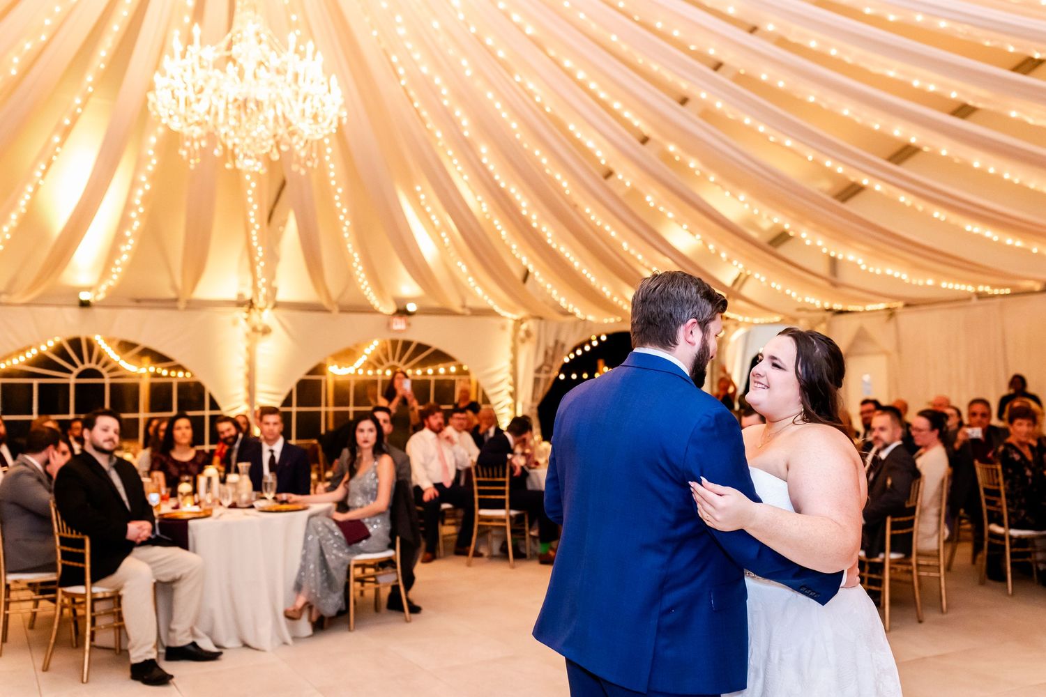 Couple shares their first dance under draped fabric ceiling and chandelier at elegant reception.