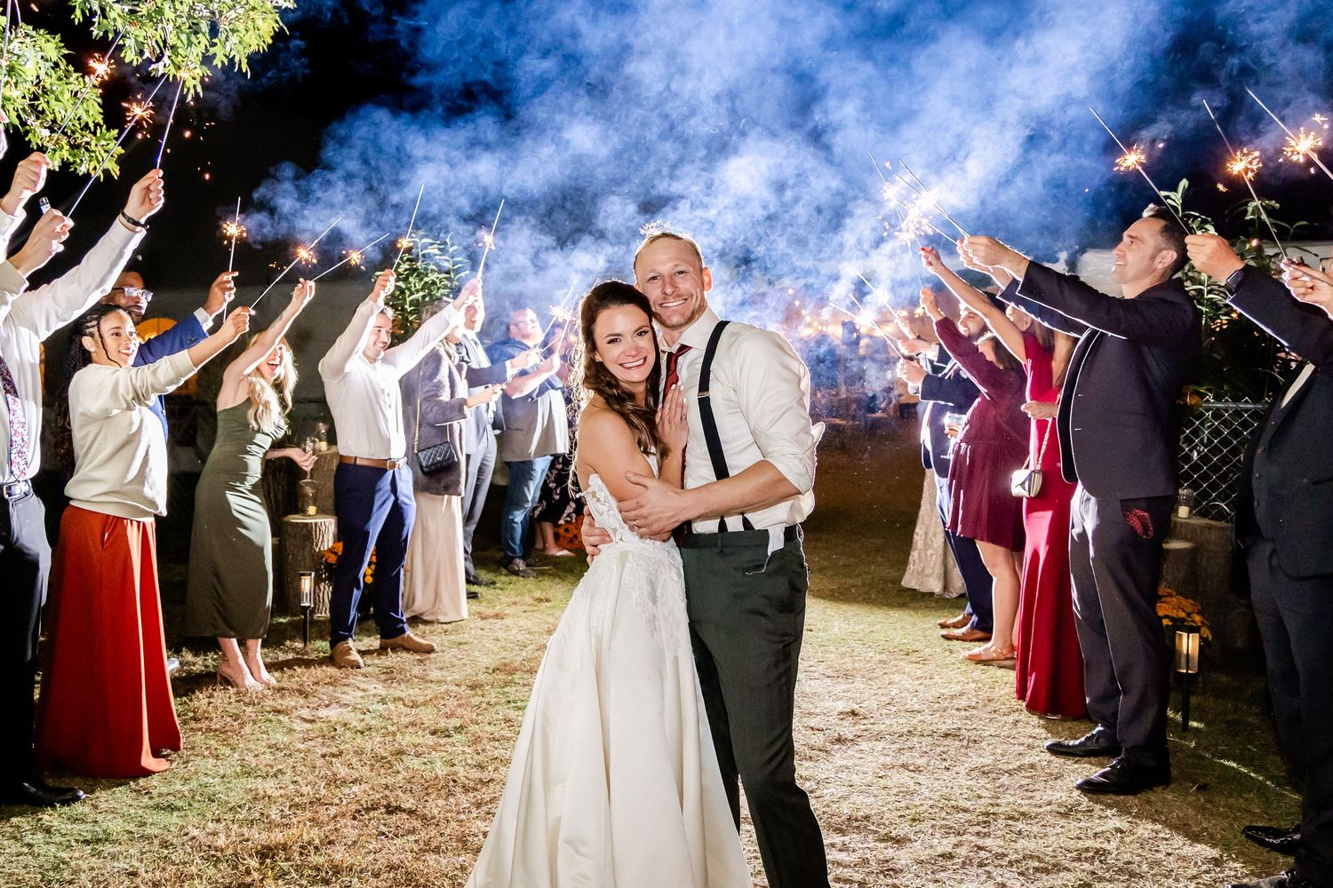 Wedding guests form an exit tunnel with sparklers for the newlyweds outdoors.