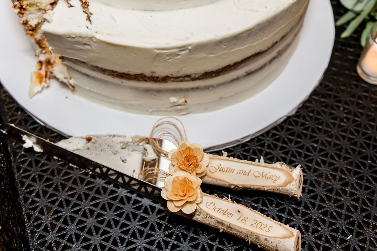 White wedding cake with gold accents and peach roses displayed on a black patterned surface.