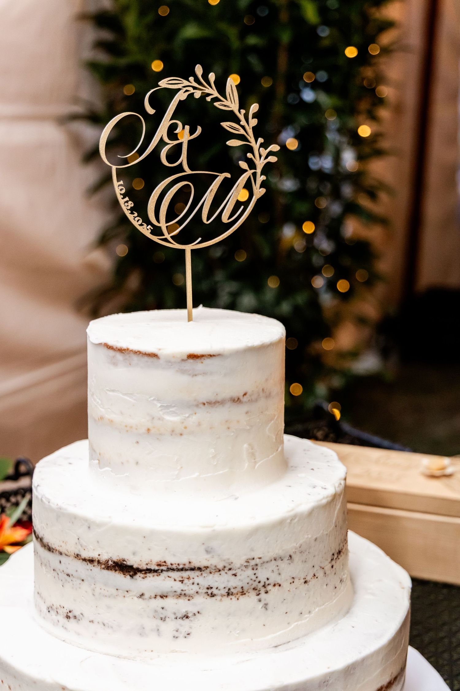 Semi-naked white wedding cake with elegant gold monogram topper.