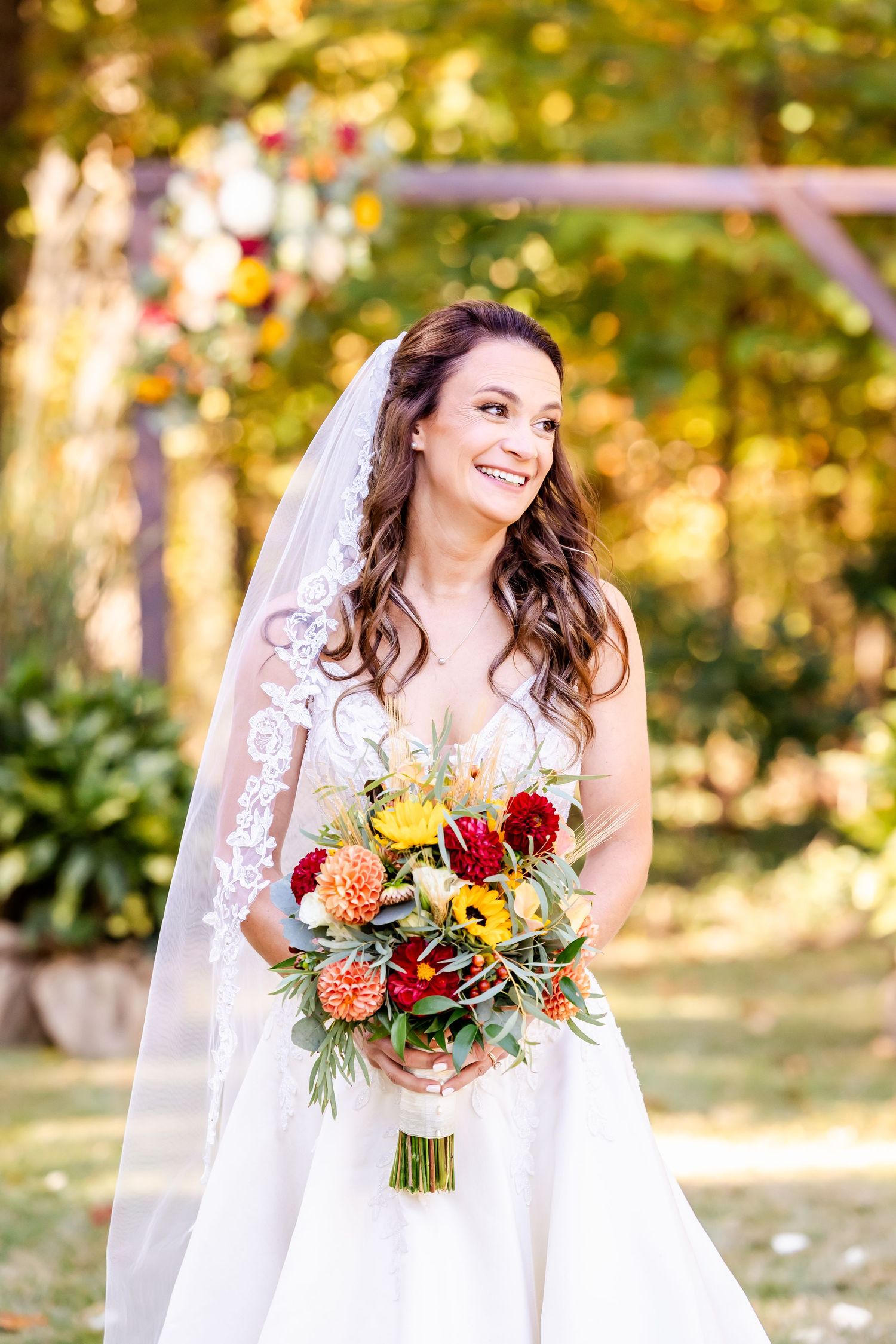 Bride holds vibrant autumn bouquet with orange and red flowers against fall foliage.
