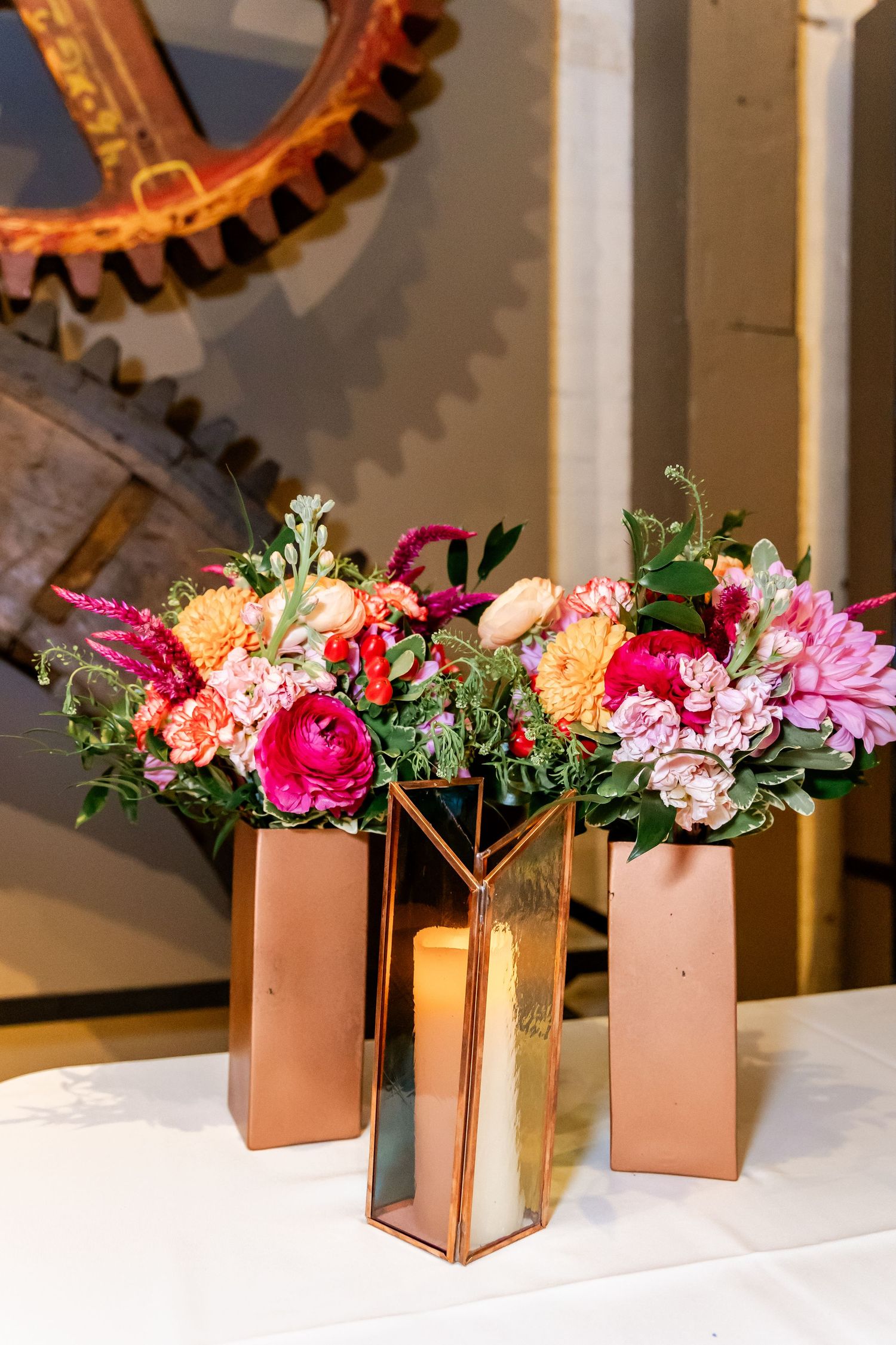Vibrant floral arrangements in copper and rose gold vases featuring pink roses, tulips and mixed flowers against an industrial backdrop.