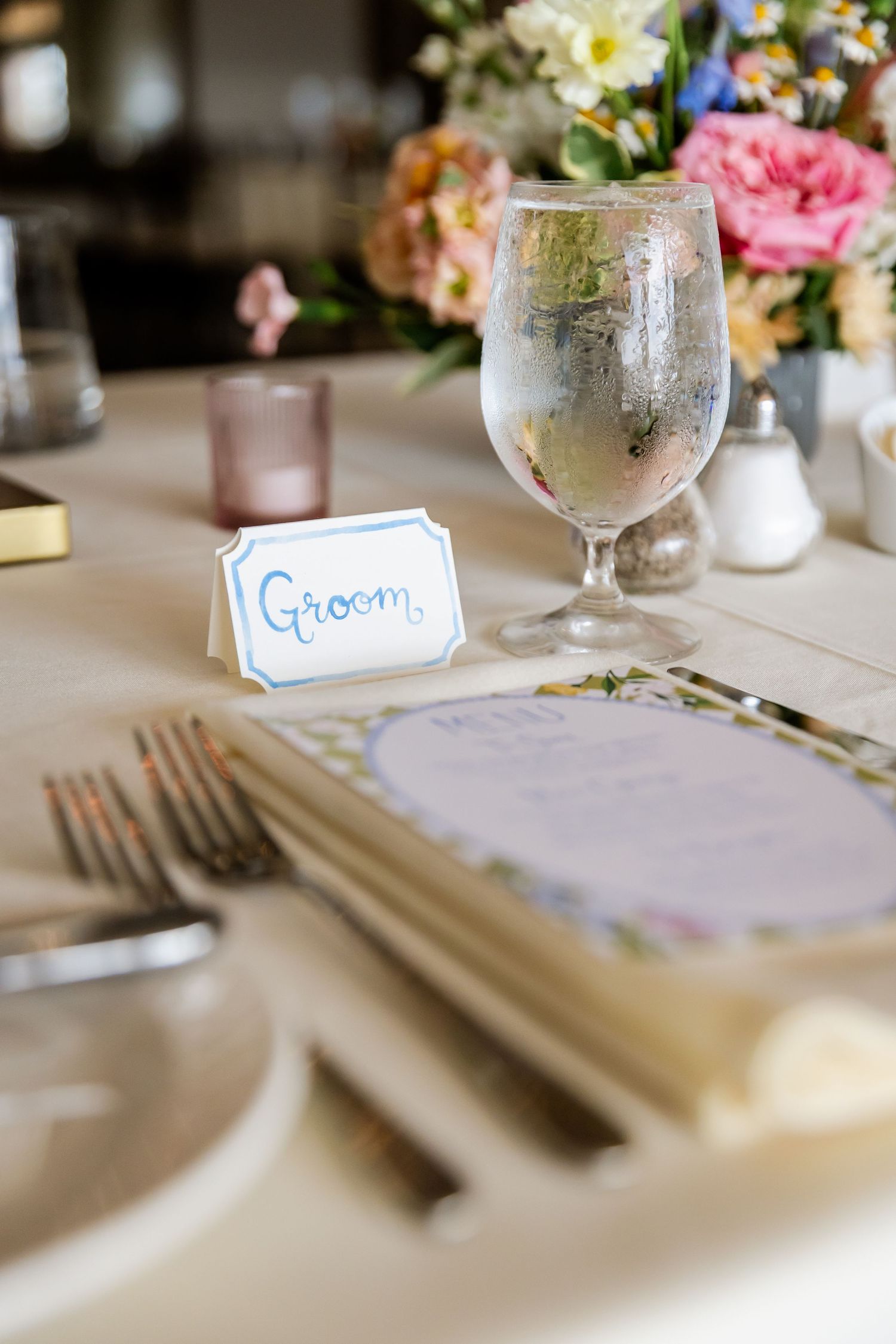 Elegant wedding reception table setting with white linens, place cards, and floral centerpieces.