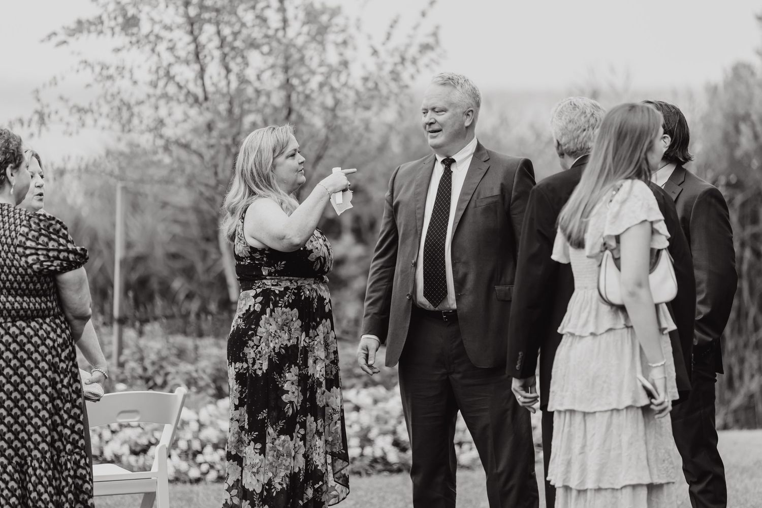 Wedding guests and wedding party gather outdoors on a grassy lawn during a summer celebration.