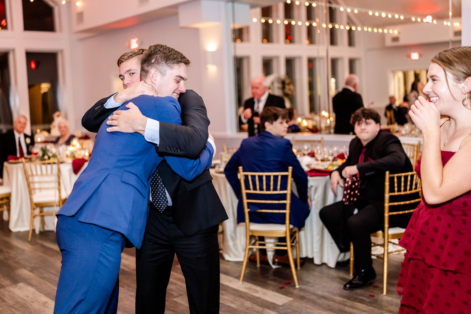 Emotional embrace between guests during wedding reception in decorated ballroom.