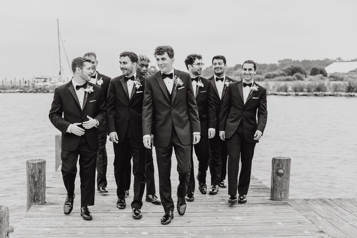 Wedding party members in formal attire walking together on a dock.