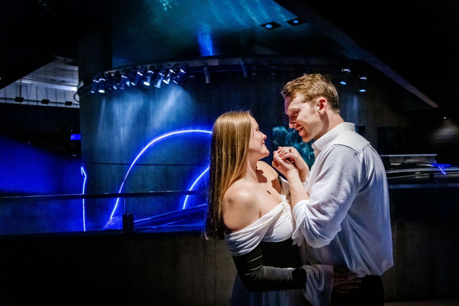 A couple shares an intimate moment under dramatic blue lighting on a stage.