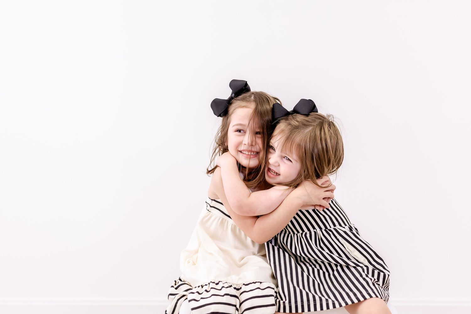 Loving mother in striped shirt holding and cuddling with young child in front of white background.