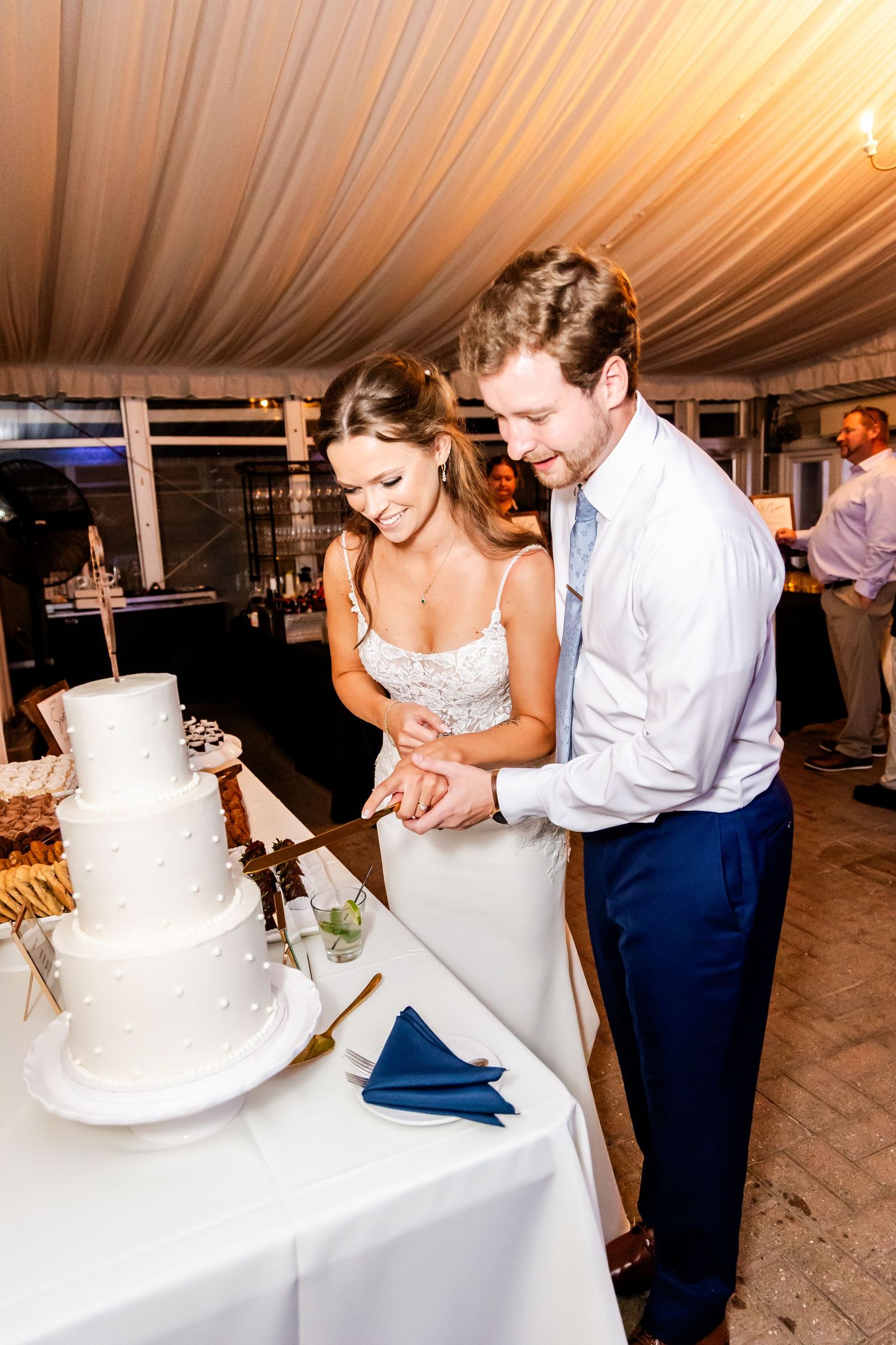 Wedding couple cutting their white tiered cake together at the reception.