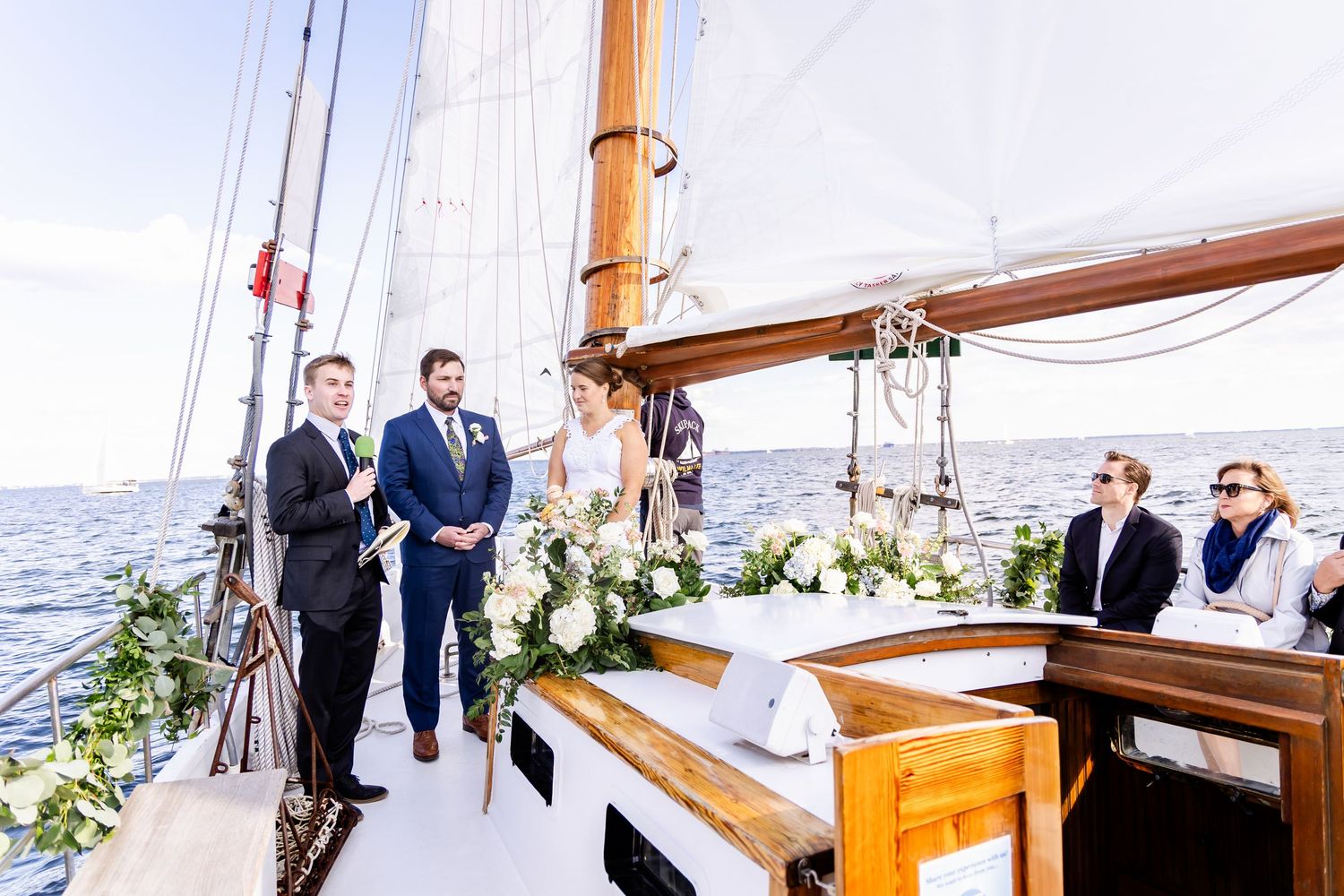 Elegant outdoor wedding ceremony on a sailboat deck adorned with white floral arrangements, overlooking the open ocean.