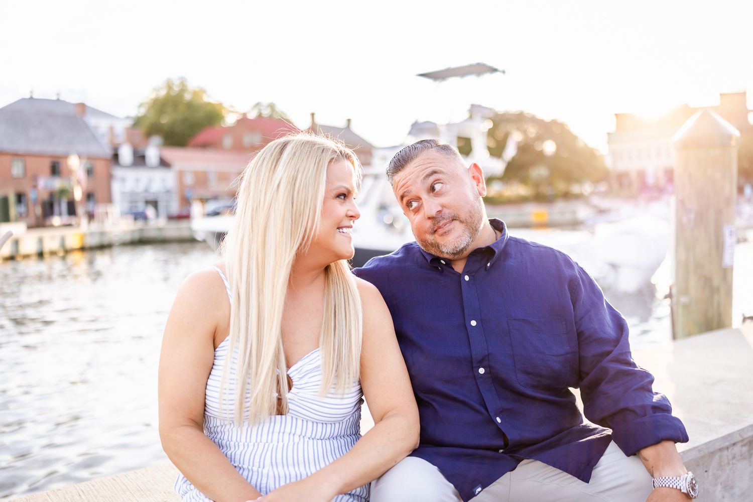Couple shares romantic moments by the waterfront during sunset engagement photo session at a marina.