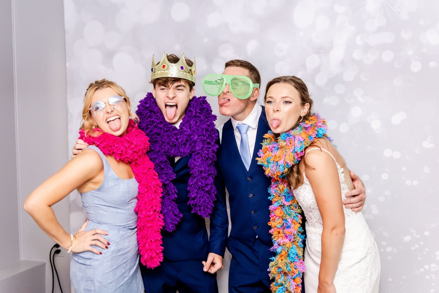 Wedding party poses with fun props and colorful boas against a sparkly backdrop.