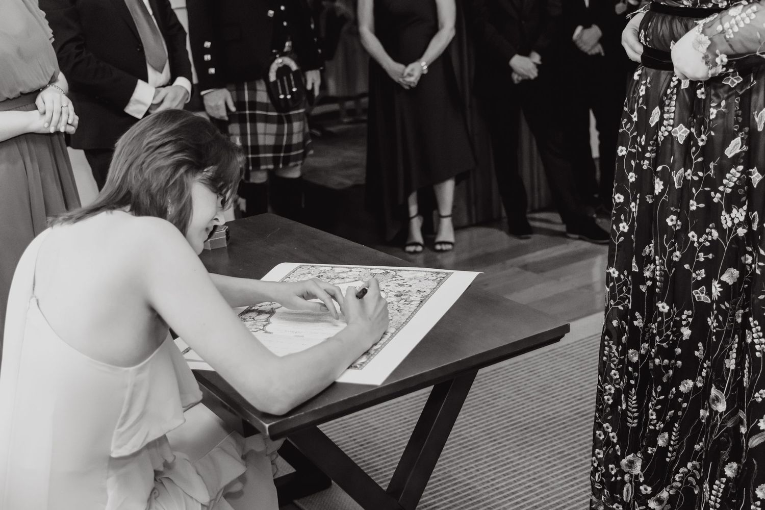 Person signing documents at a wooden table during an indoor event.