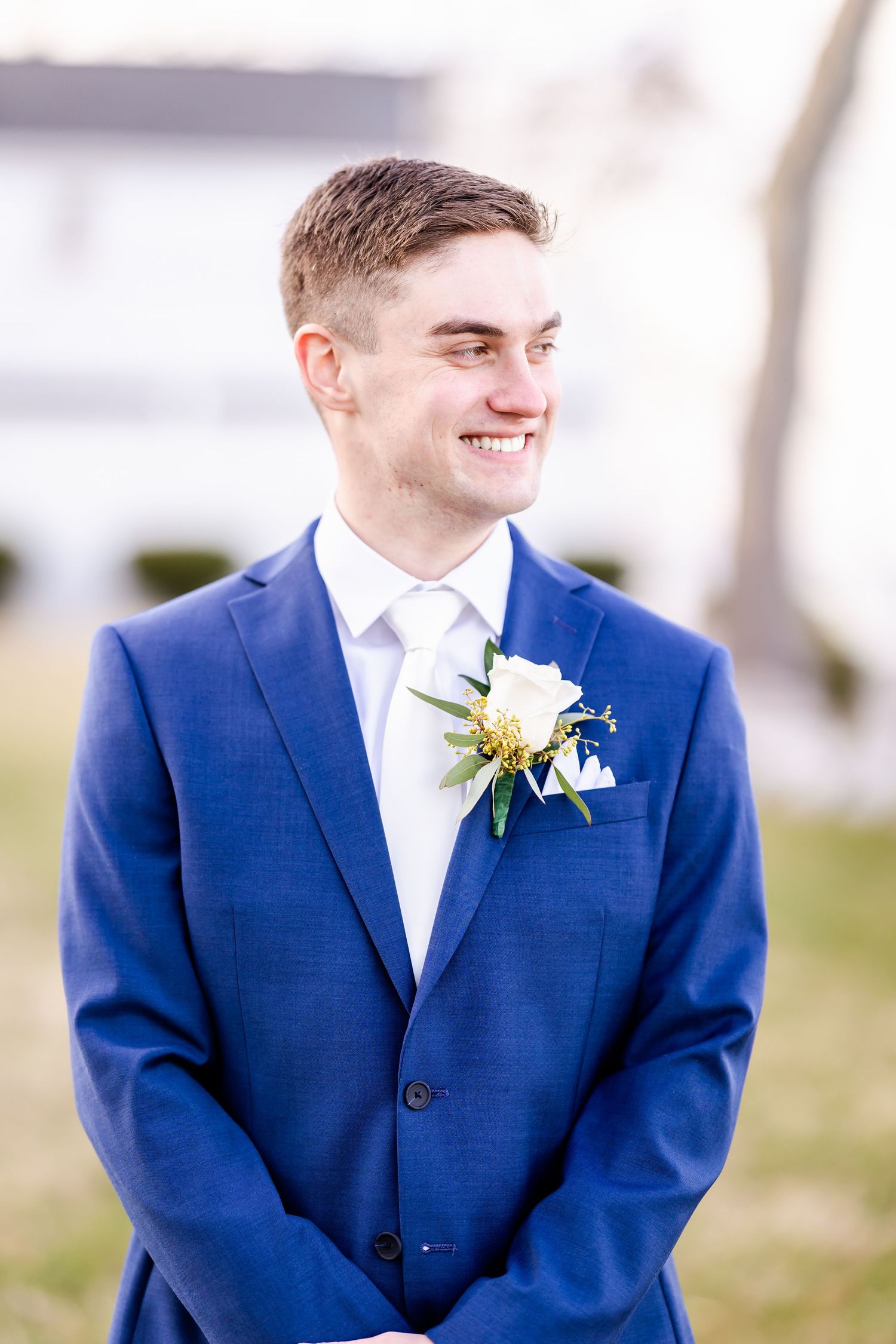 Groom wearing navy blue suit and boutonniere smiles during outdoor wedding portraits.