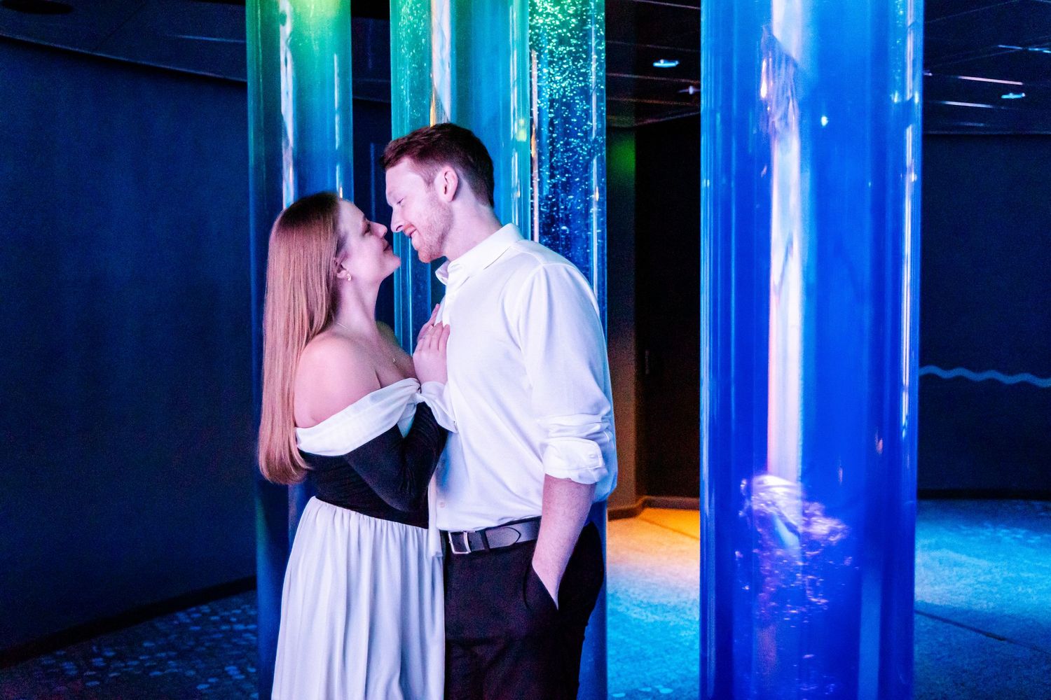 A romantic couple shares an intimate moment near glowing blue columns in a dark, atmospheric setting.