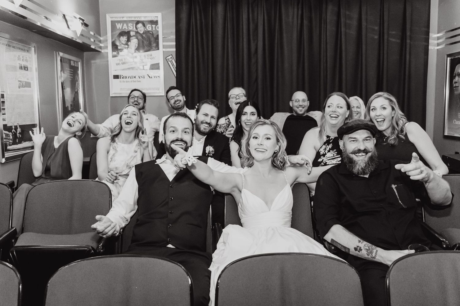 Wedding party sitting together in theater seats showing playful expressions and gestures in black and white.