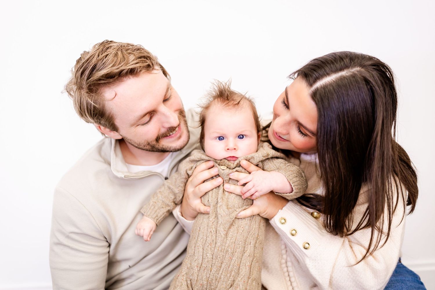 Joyful family moment captured with warm smiles and laughter against white backdrop.