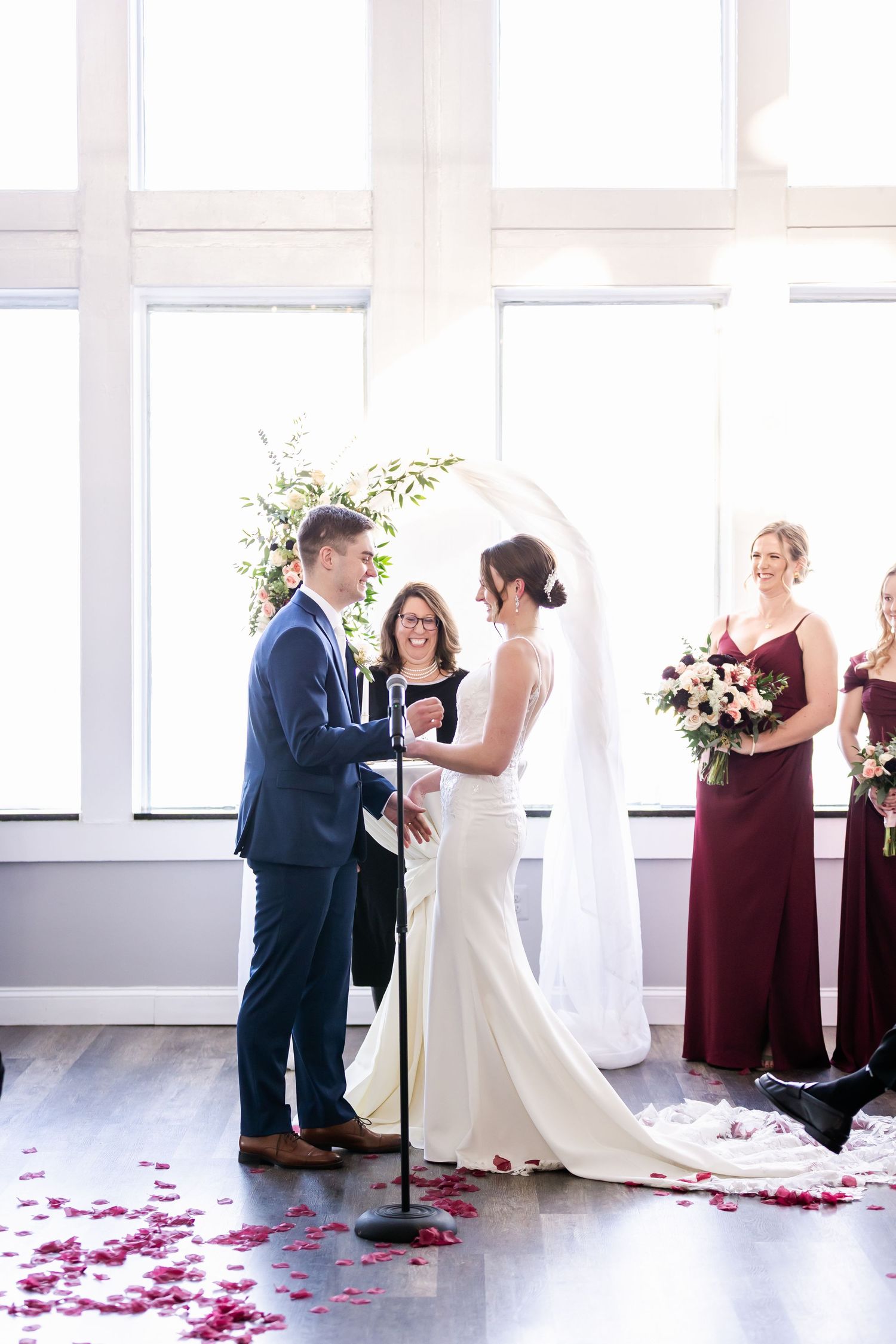 Indoor wedding ceremony space with white windows, rose petals, and burgundy accents.