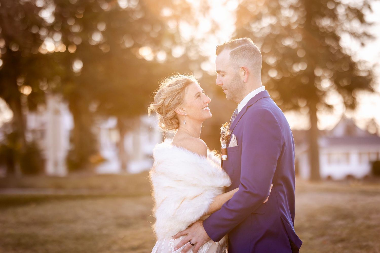 A romantic sunset wedding portrait of a couple embracing outdoors with warm golden light filtering through trees.