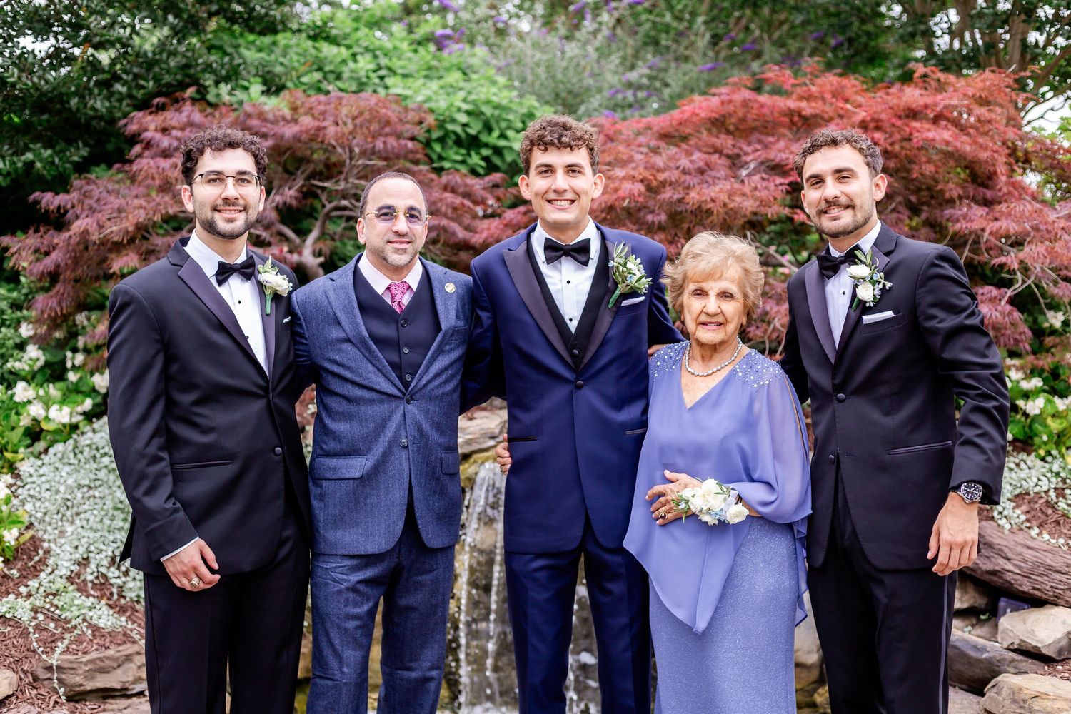 Wedding party in formal attire posing against backdrop of vibrant red Japanese maple trees.