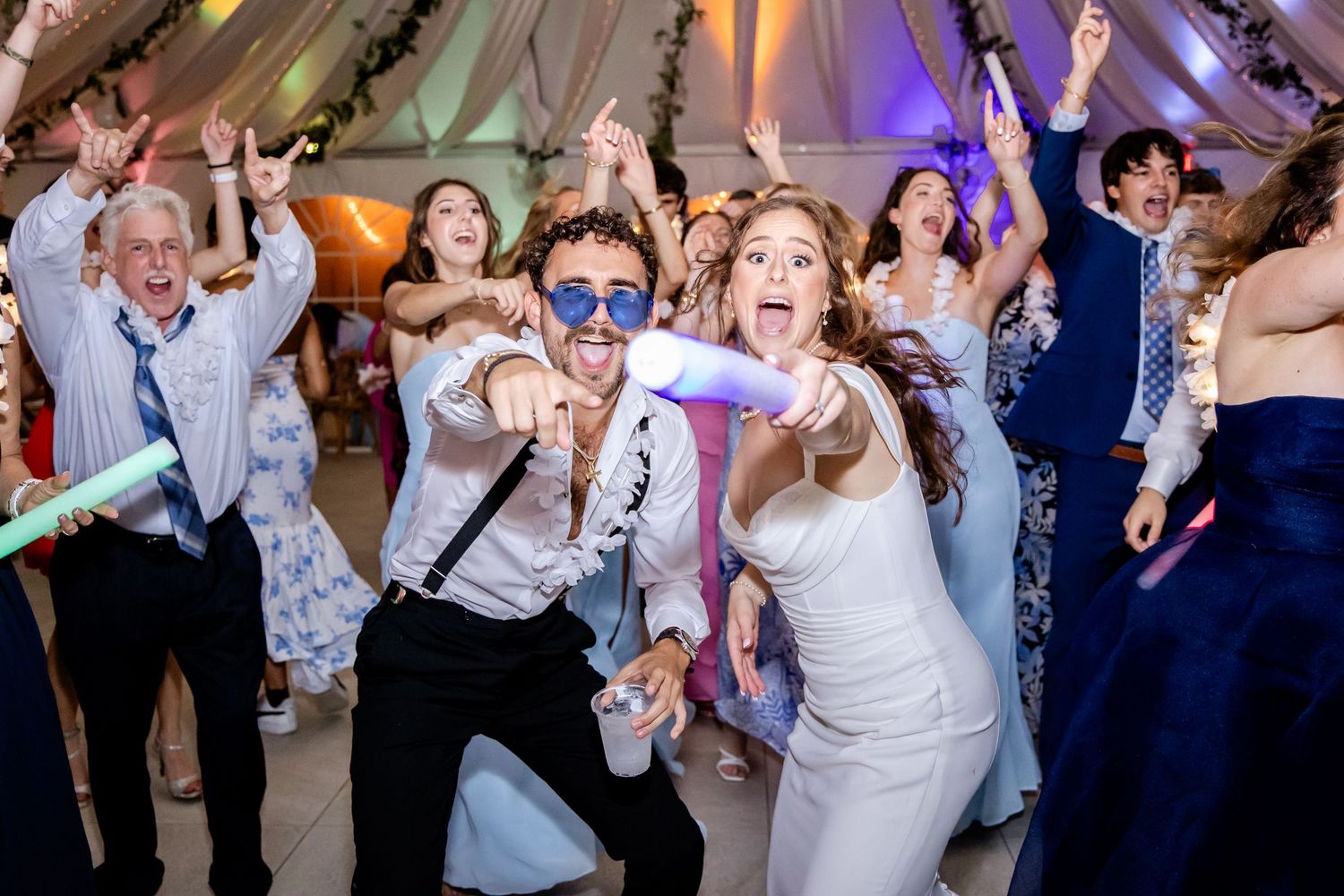 Wedding celebration with guests dancing energetically under colorful lighting.
