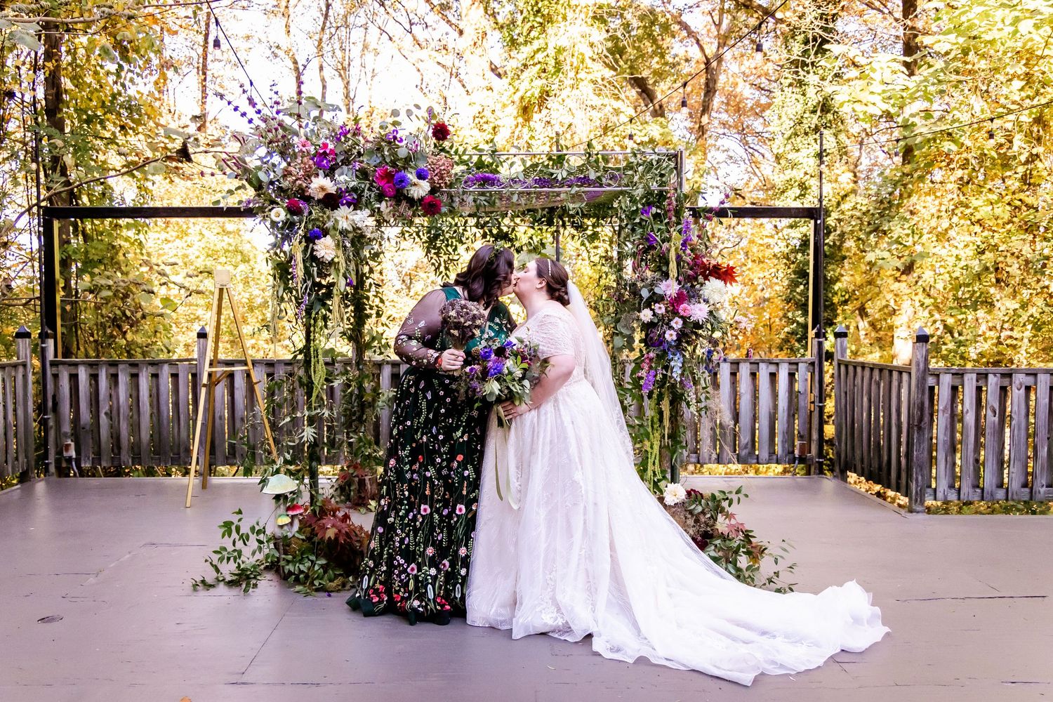 Outdoor wedding ceremony setup with floral arch and purple flower arrangements.