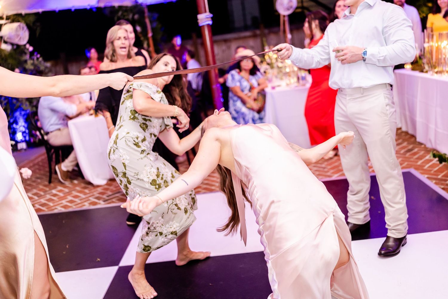 Wedding guests dancing and having fun on the dance floor at a reception with purple lighting.