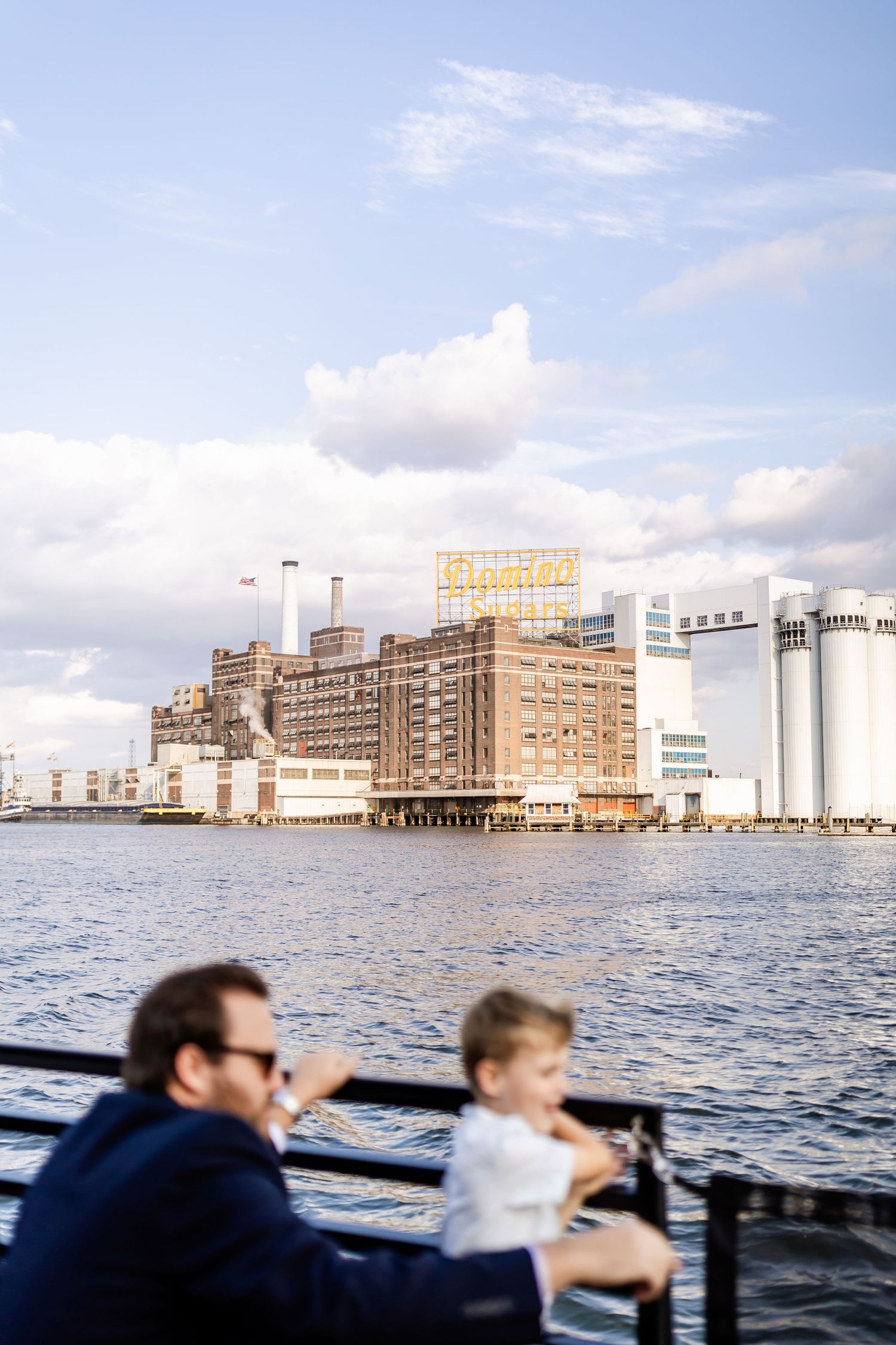 Two figures enjoy a waterside view of industrial buildings and grain silos along the waterfront.