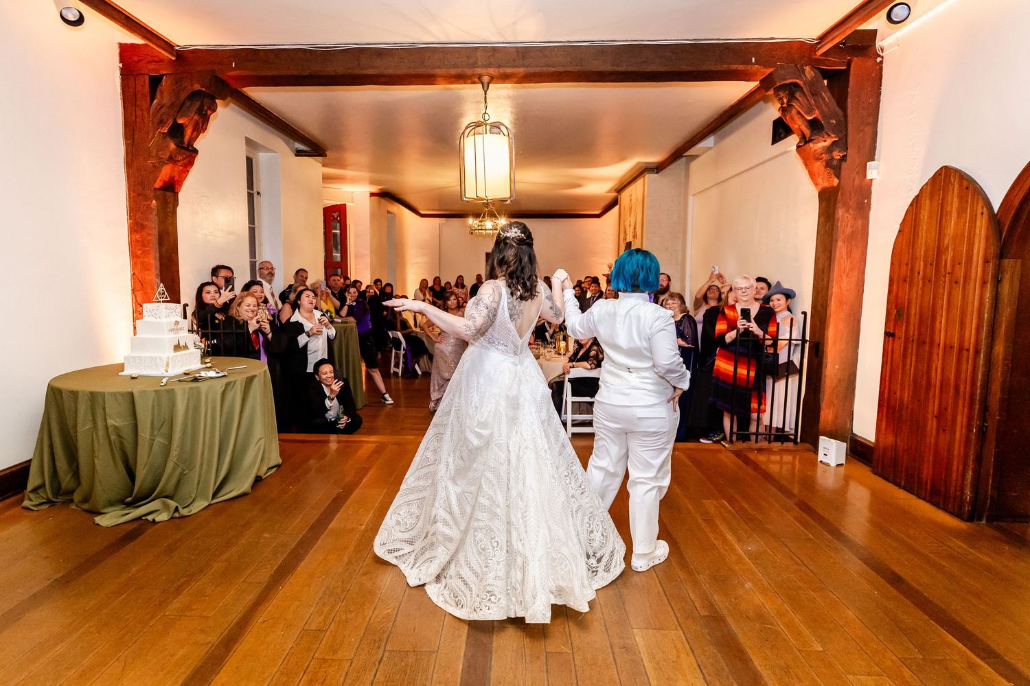 A couple makes their grand entrance into a rustic wooden reception hall filled with guests.