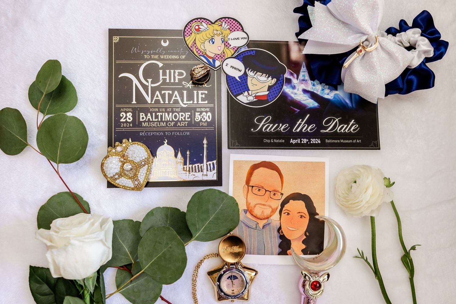 Wedding stationery and decorative items arranged with white roses and greenery.