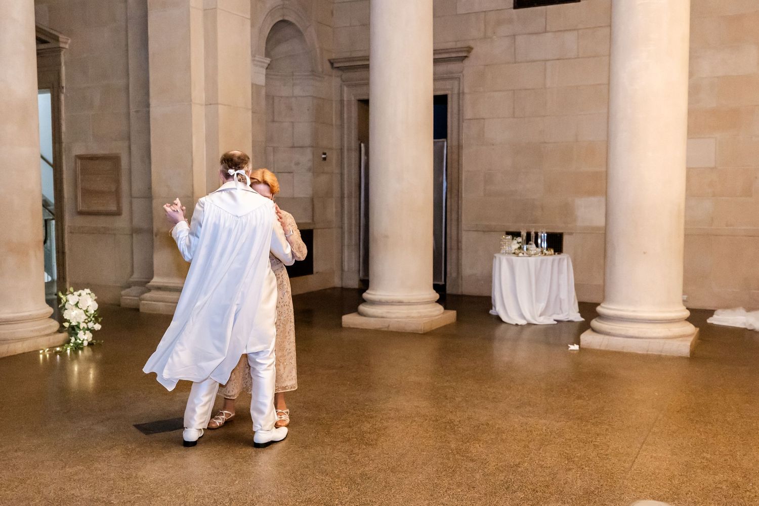 Two people dance together in a grand hall with classical stone columns and decorative elements.