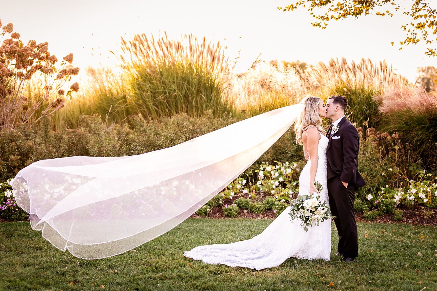 A sunset wedding photo with the bride's long veil dramatically flowing in the wind.