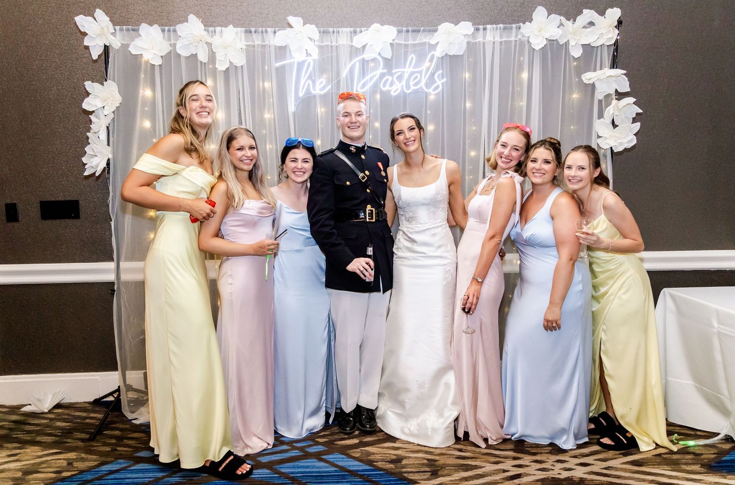 Wedding party members in pastel dresses and formal attire posing together at elegant venue.