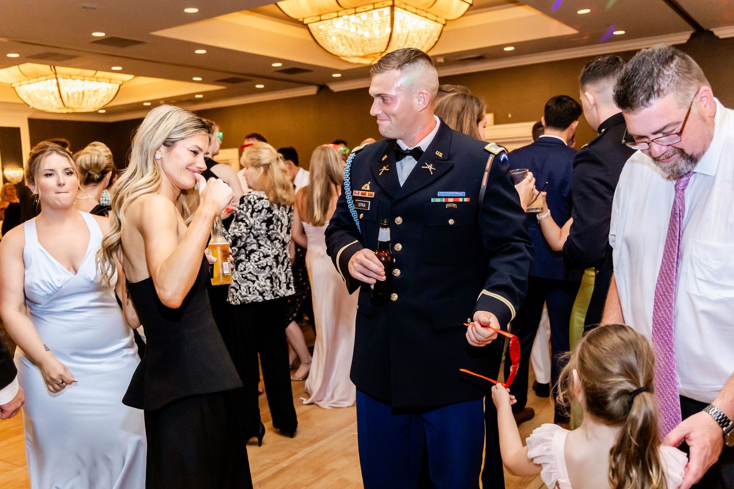 Wedding reception guests enjoying lively conversation and dancing under elegant chandeliers.