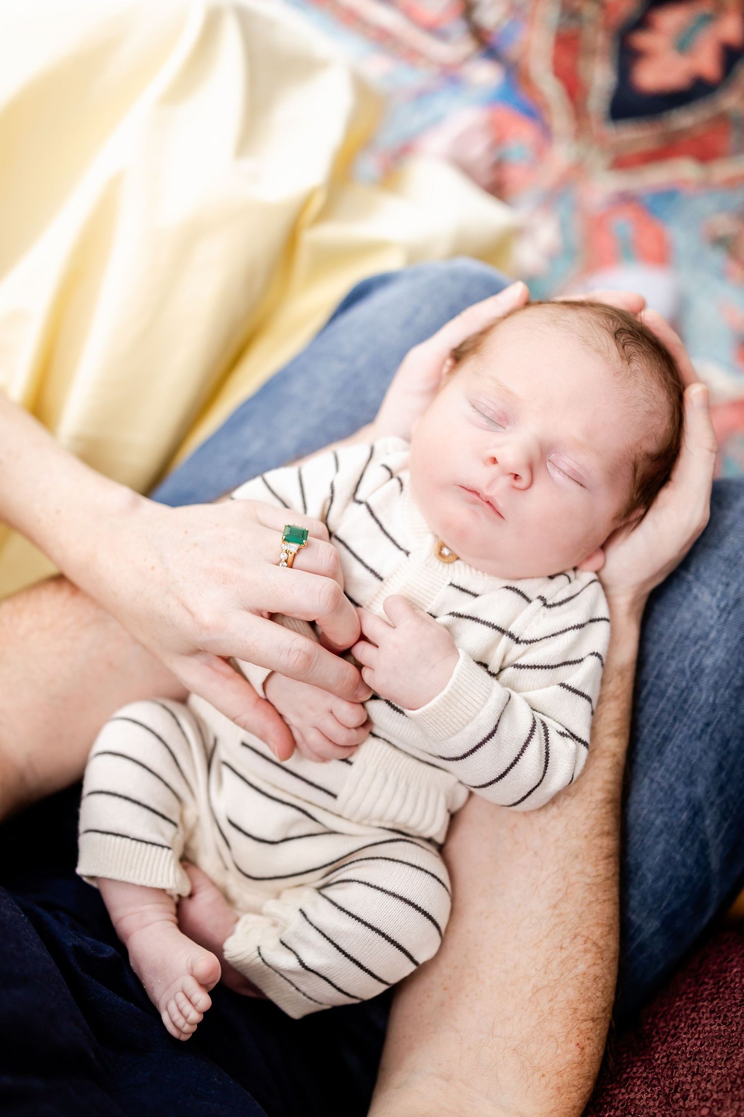 Sleeping newborn in striped onesie being cradled on patterned blanket.