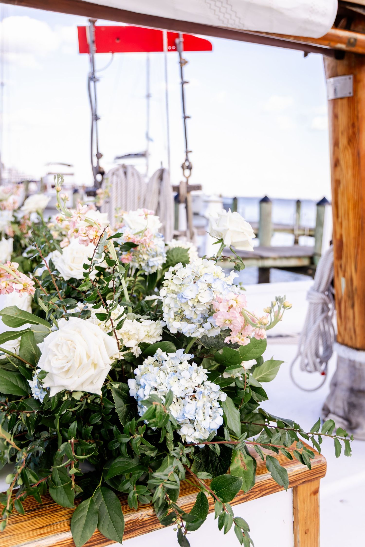 Elegant floral arrangement of white roses and blue hydrangeas on a wooden boat dock at a marina.