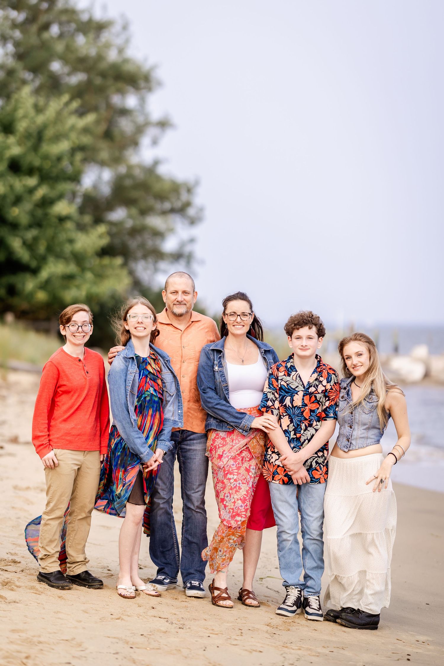 Group wearing colorful casual outfits poses together on sandy beach.