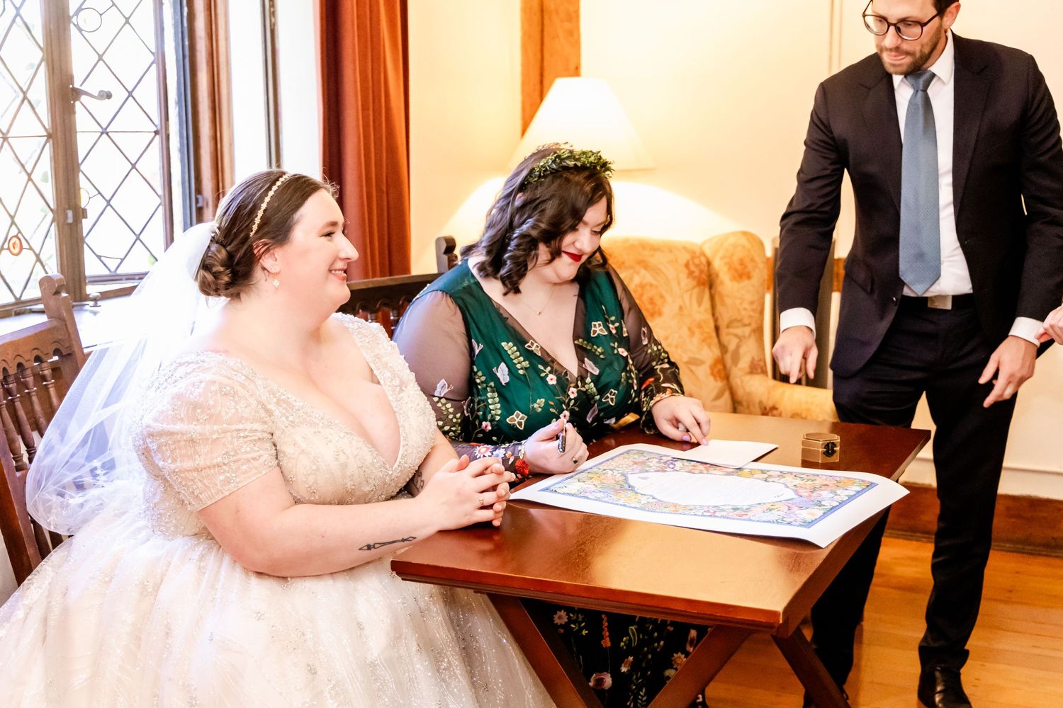 Wedding ceremony signing with people gathered around table in elegant indoor setting.